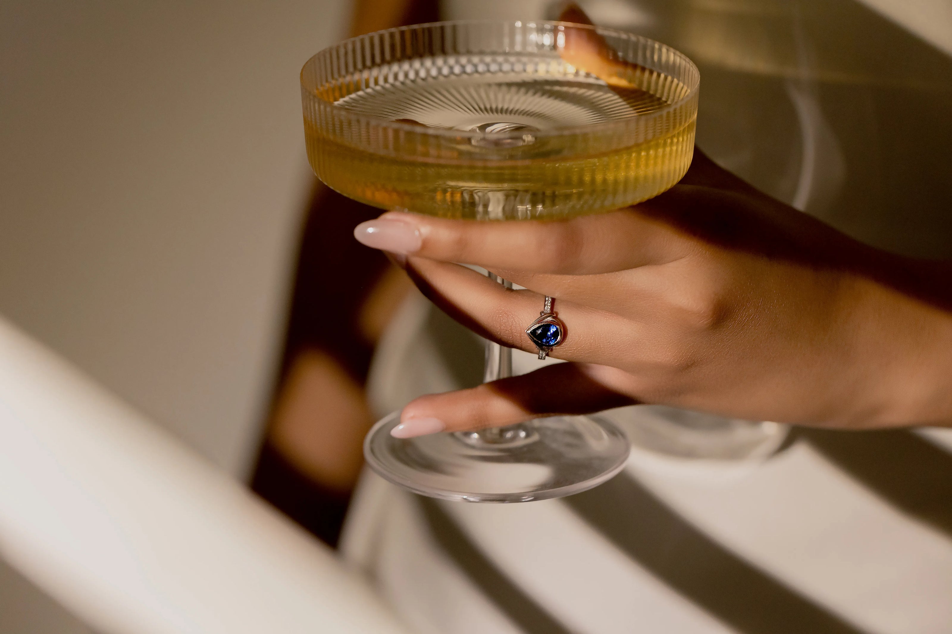 Blue sapphire ring in white gold with diamonds, paired with a champagne glass, celebrating love and sophistication.