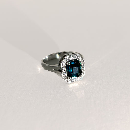Art Deco-style 18K white gold ring featuring a 1.56ct emerald-cut unheated teal sapphire, surrounded by a halo of diamonds, offering a bold, timeless statement.