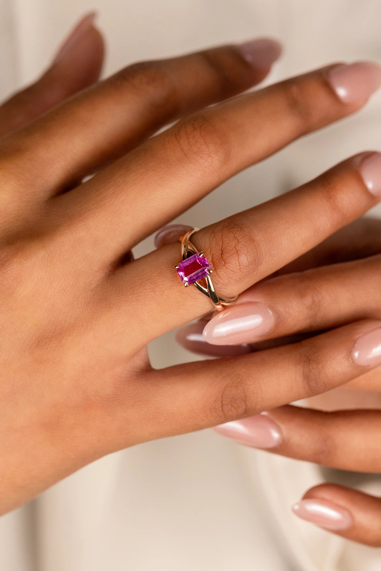18K yellow gold engagement ring with 1.1ct unheated Emerald cut Pink Sapphire from Sri Lanka, set in a playful criss-cross design, celebrating individuality and style.