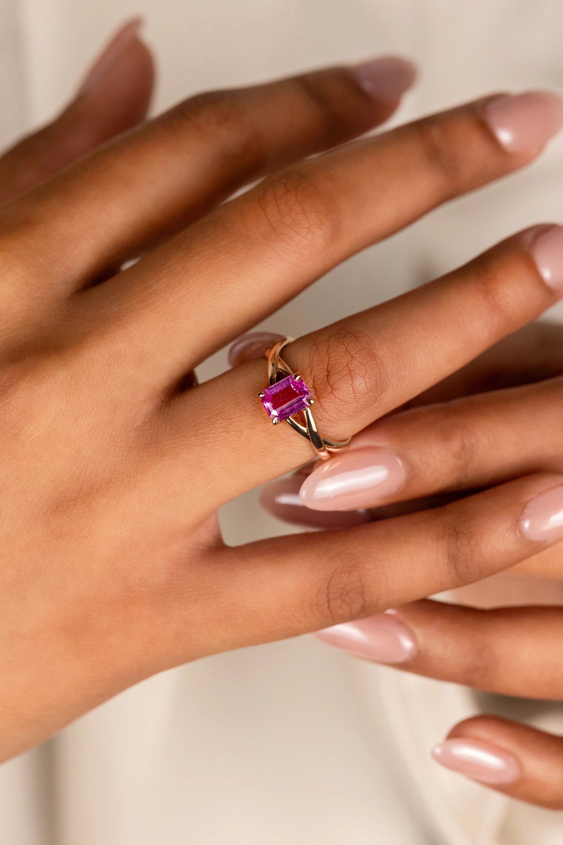 18K yellow gold engagement ring with 1.1ct unheated Emerald cut Pink Sapphire from Sri Lanka, set in a playful criss-cross design, celebrating individuality and style.