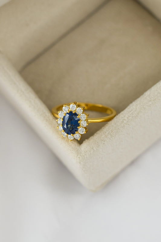 Princess Diana-inspired blue sapphire cluster ring with 1.36ct sapphire and 14 VVS1 diamonds, handcrafted in yellow gold.
