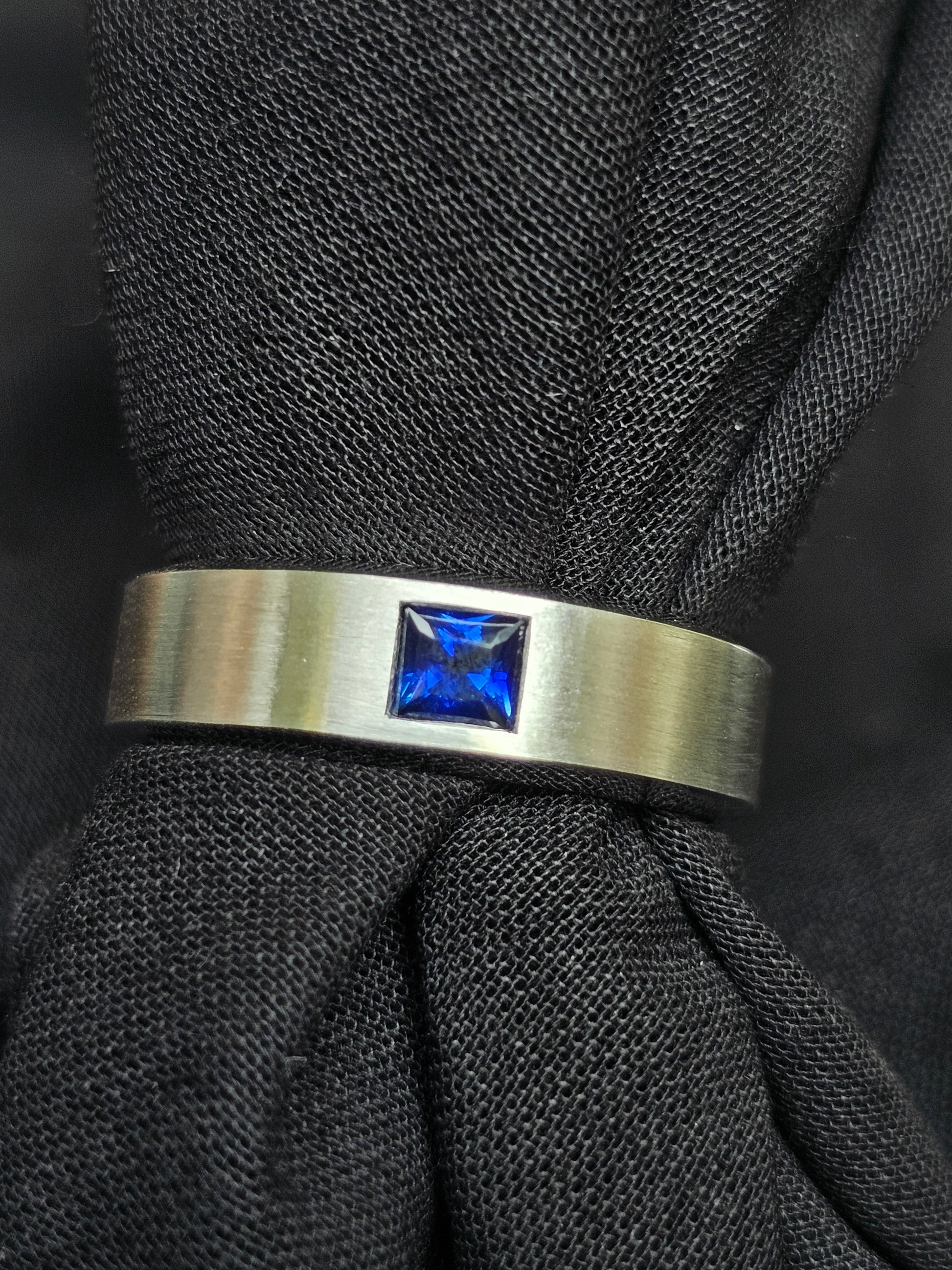 18K white gold band with a matte finish, crafted with a princess-cut Royal Blue Sapphire, symbolizing love and connection.