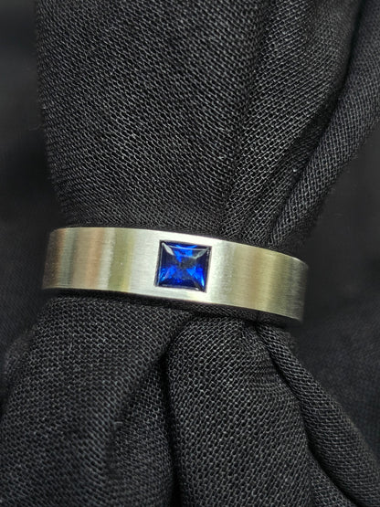 18K white gold band with a matte finish, crafted with a princess-cut Royal Blue Sapphire, symbolizing love and connection.