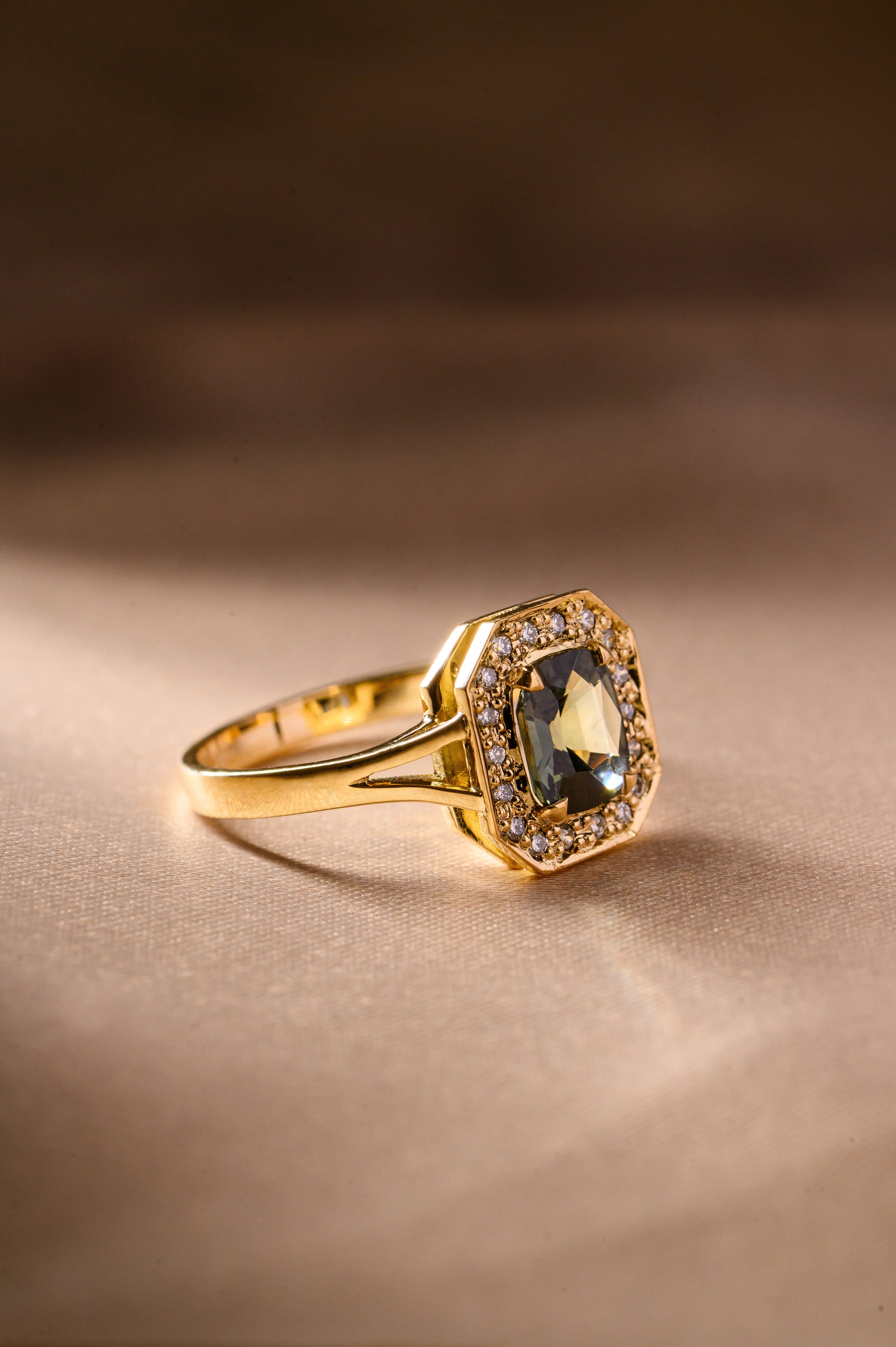 Luxury sapphire engagement ring featuring a teal green sapphire, diamonds, and a yellow gold band.